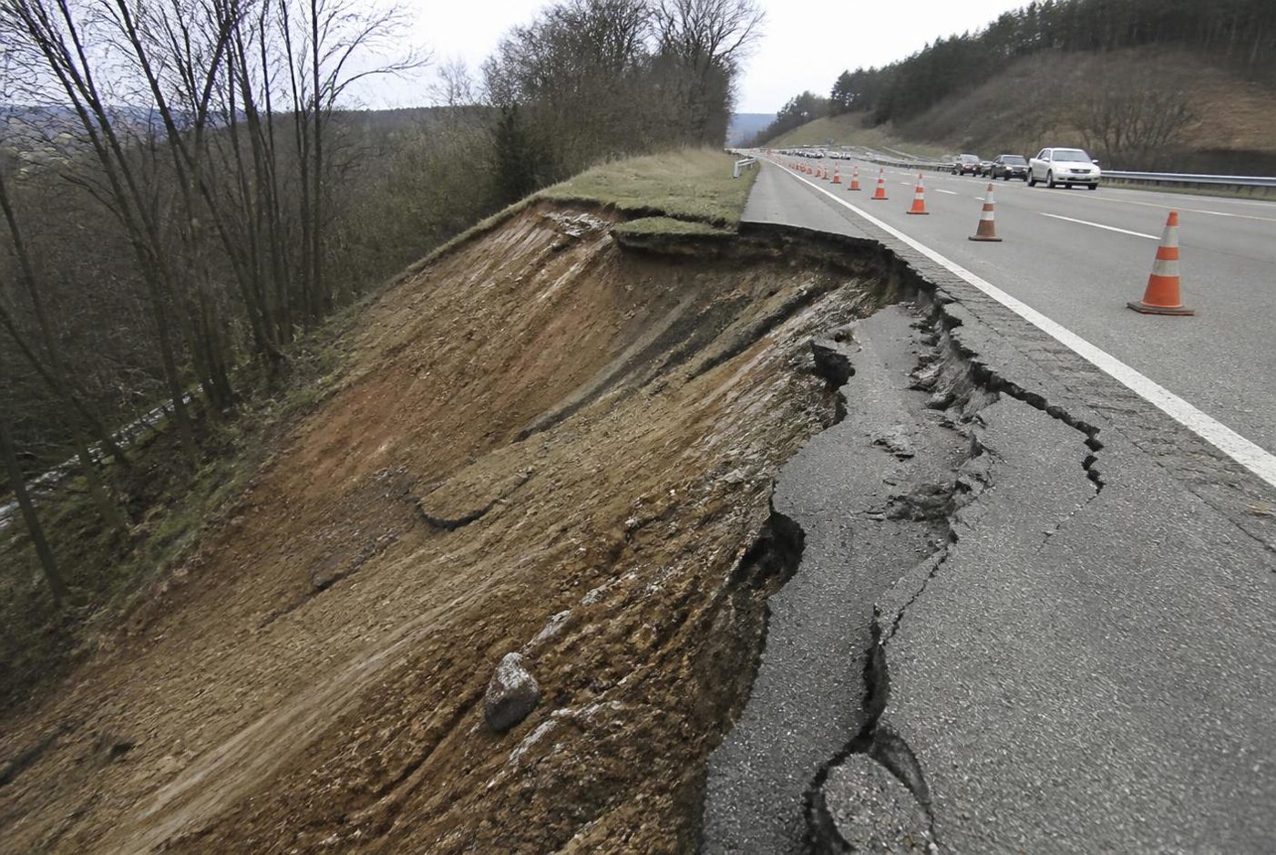 Rotational slope failure along a highway embankment with a scarp and cracked shoulder.
