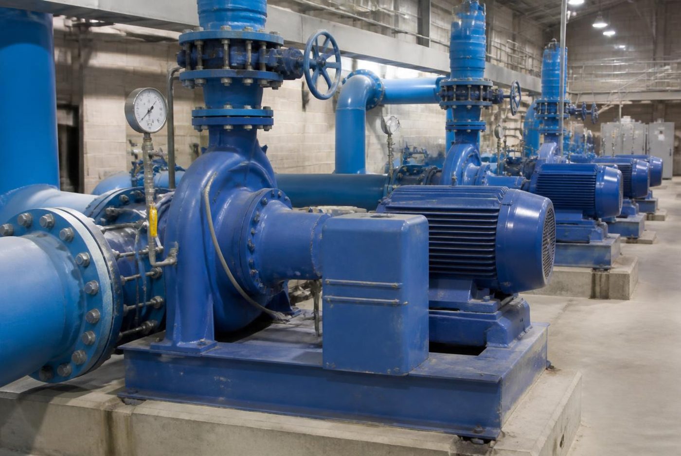 Row of centrifugal pumps and valved steel piping inside a water pumping station.