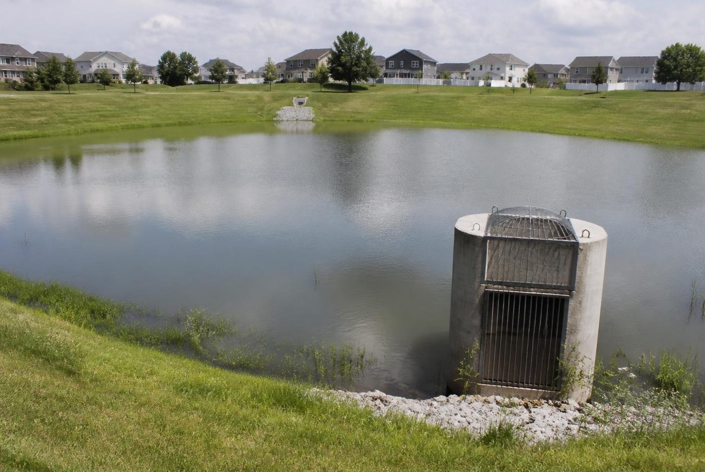 Stormwater detention basin holding water, with a concrete outlet riser and trash rack.