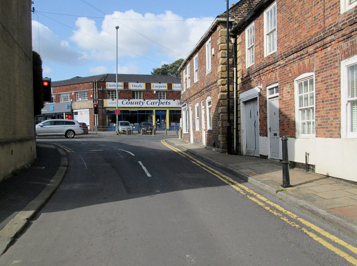 Signalized urban street junction with traffic signals, markings and parked vehicles.