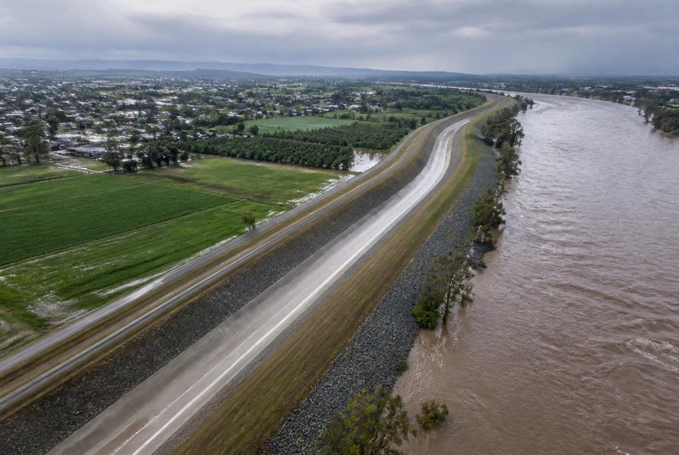 Aerial view of an earthen levee with riprap protection alongside a swollen river.
