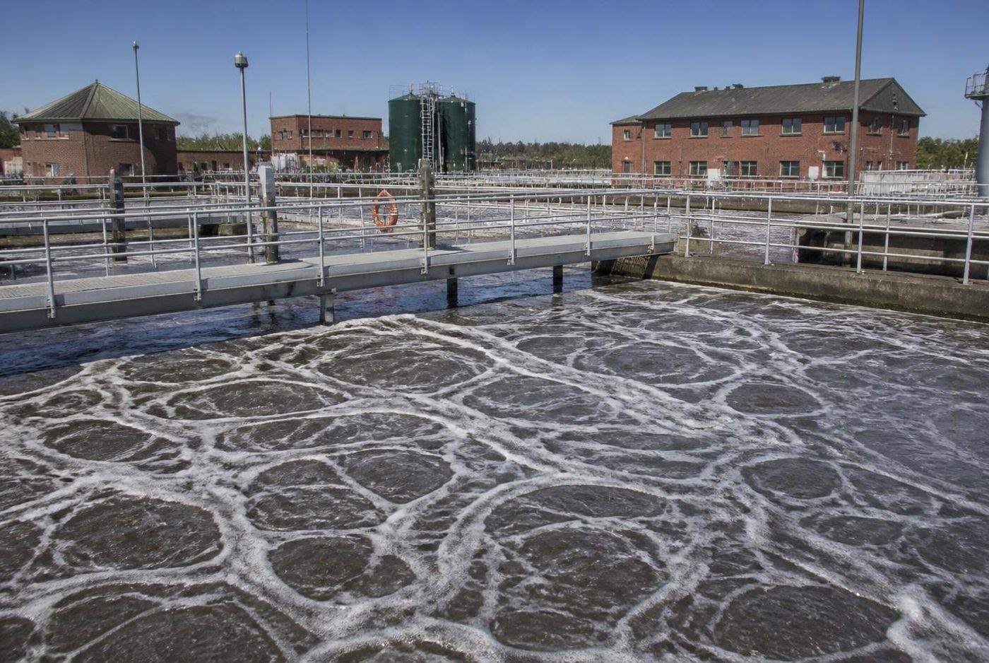 Aeration basin at a wastewater treatment plant with churning aerated water and walkways.